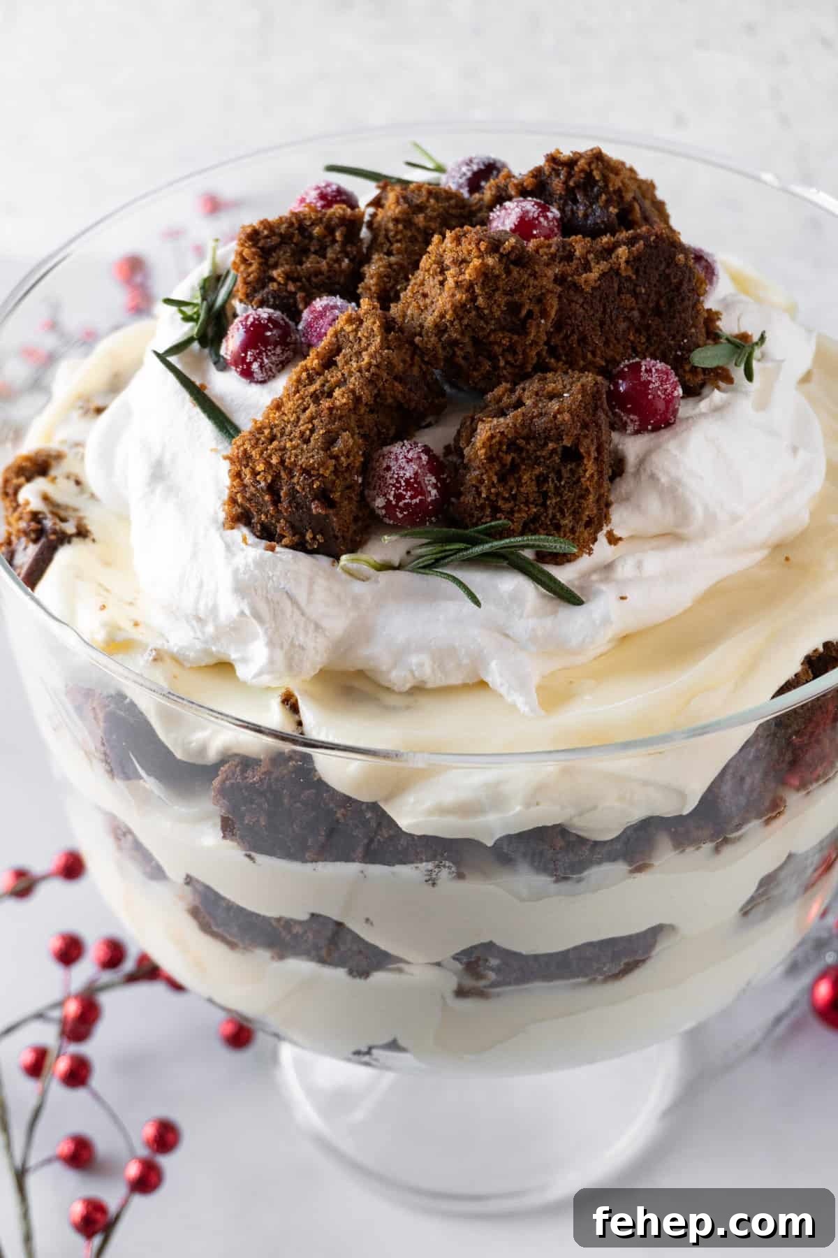 Gingerbread Trifle Recipe: Festive Layered Dessert for Holidays 18 Gingerbread Trifle in Trifle dish showing beautiful distinct layers of cake, pudding, and whipped topping fluff. Cranberry decorations around base of dish.
