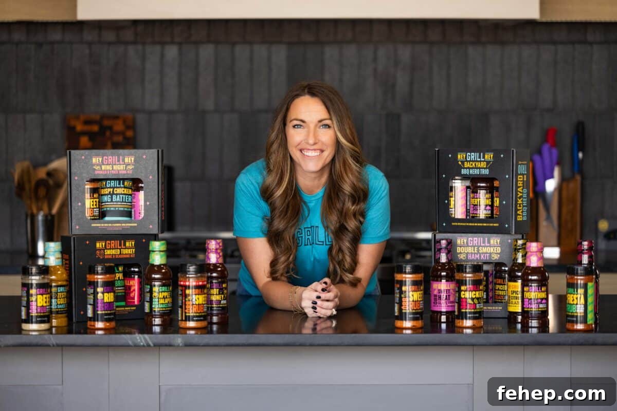 Perfect BBQ Gift Ideas for the Grillmaster This Season 5 Susie from Hey Grill Hey leaning over a counter topped with her product lineup.