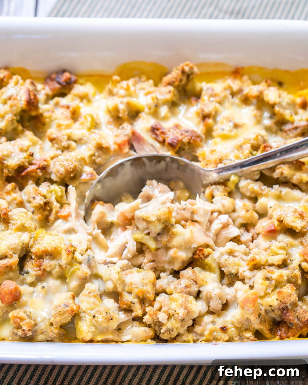 Simple 3-Step Leftover Turkey Casserole Recipe 2 3/4 view of a turkey casserole in a white dish showing creamy turkey and dressing with a spoon dipping in.