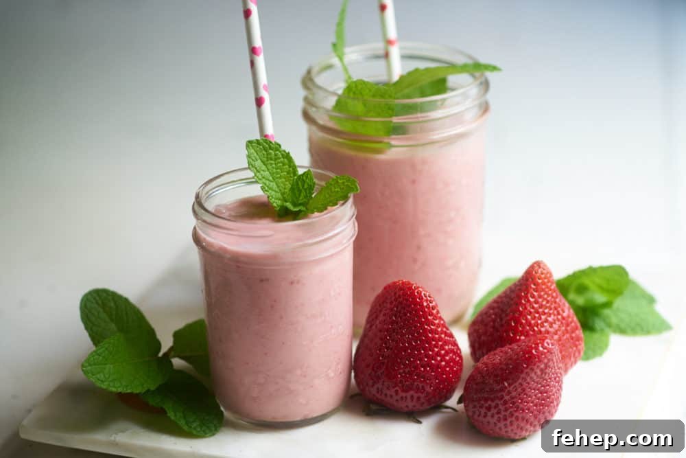 Creamy Dairy-Free Strawberry Milkshake Recipe 6 Two strawberry dairy-free milkshakes with straws and sprigs of mint on a tray with fresh strawberries.