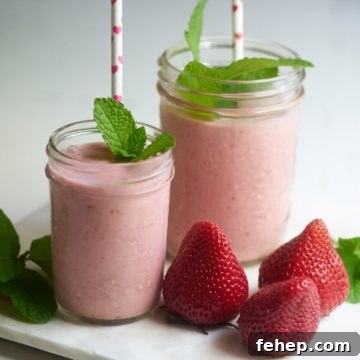 Creamy Dairy-Free Strawberry Milkshake Recipe 7 Two strawberry dairy-free milkshakes with straws and sprigs of mint on a tray with fresh strawberries.