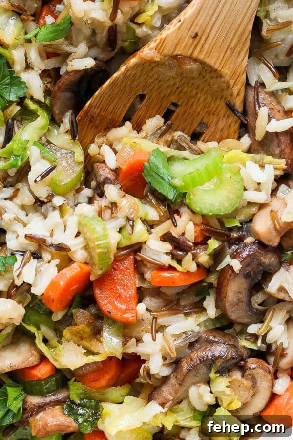 Wooden spoon in a pan of wild rice pilaf with carrots and parsley.