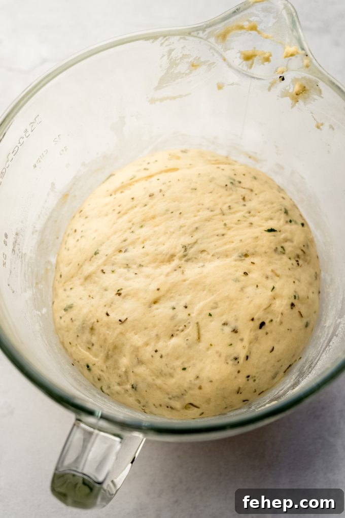 Herbed dinner roll dough that has rise in a glass bowl.