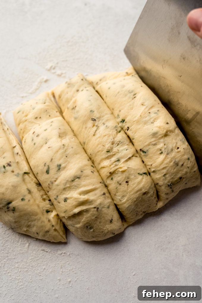 Someone is cutting herbed dinner roll dough with a bench scraper.