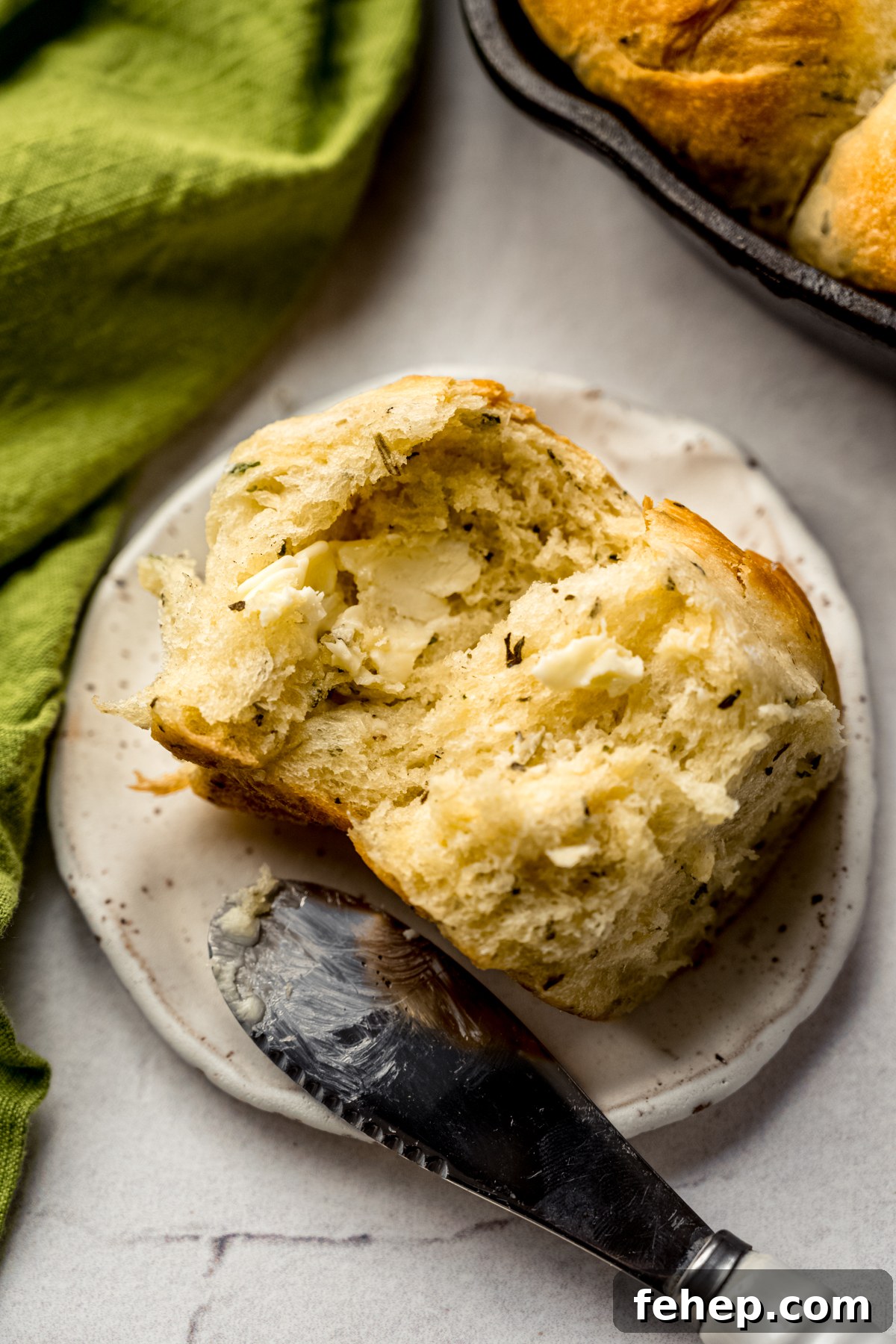 An herbed skillet roll that has been spread with butter on a plate with a spreader.
