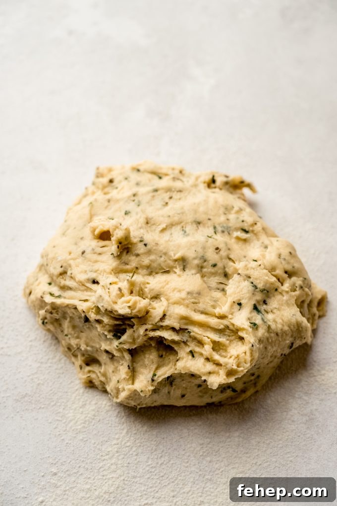 A ball of herbed dinner roll dough on a surface before it has been kneaded.