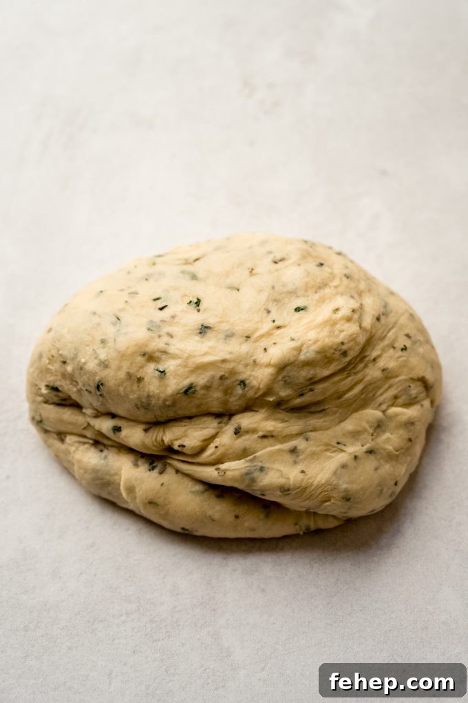 A ball of herbed dinner roll dough on a surface.
