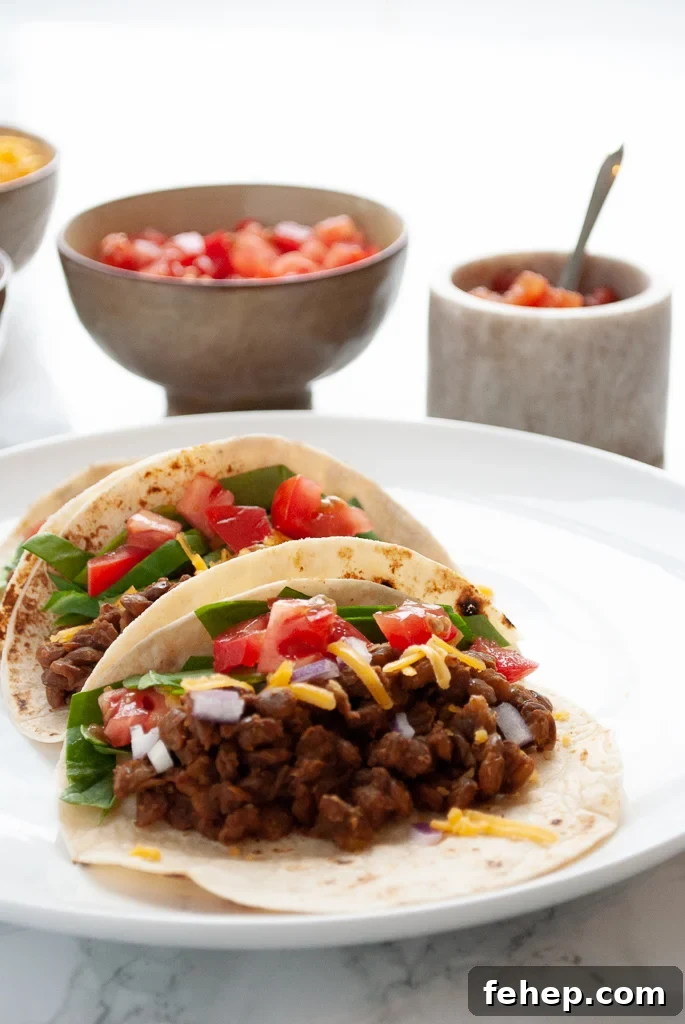 A plate of three instant pot lentil tacos with toppings in the background.