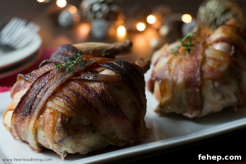 Bacon-Wrapped Cornish Hens with 3 Simple Ingredients 6 Bacon wrapped cornish game hens with plates in the background.