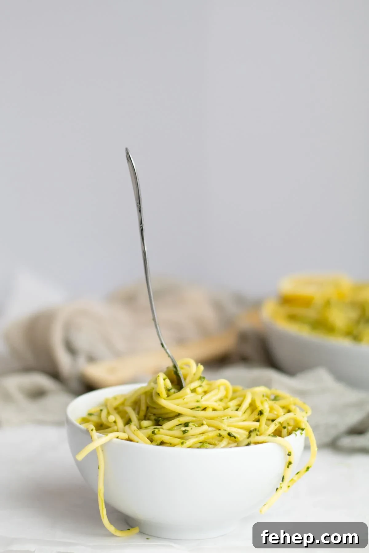 spinach pesto pasta in a white bowl with a fork standing up