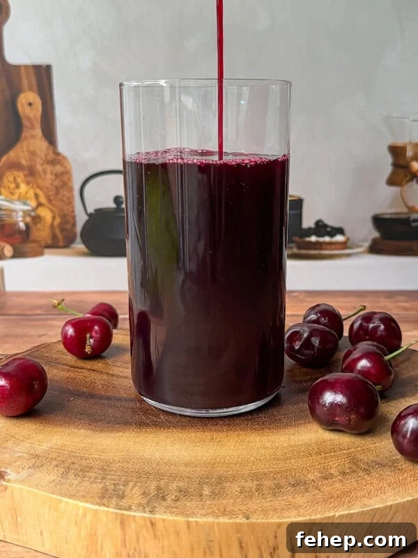 A glass is being filled with dark red cherry juice, placed on a wooden board with several fresh cherries around it.
