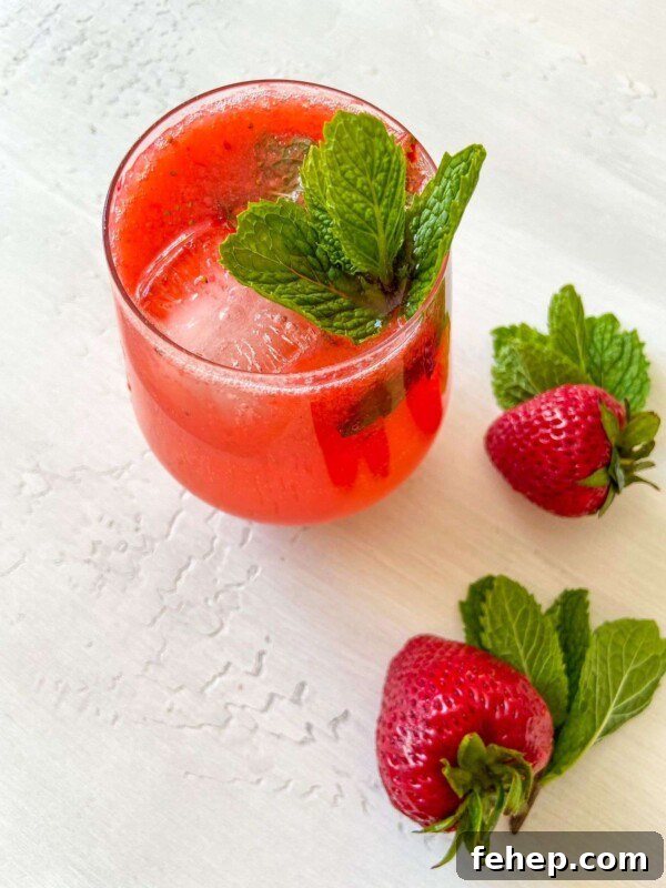 A glass of Strawberry Mojito with ice, garnished with fresh mint leaves.