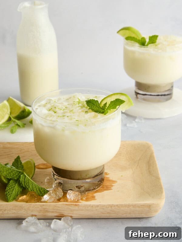 A creamy white drink garnished with lime and mint is served in a glass on a wooden board.