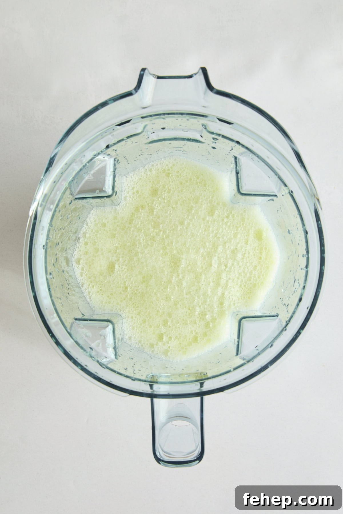Top-down view of a blender with Brazilian Lemonade - a light green, frothy liquid.