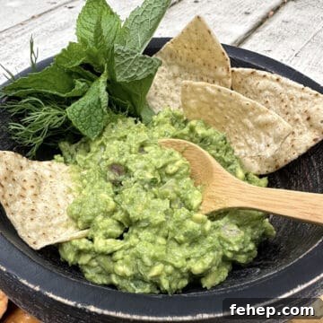 A serving of guacamole with fresh herbs and chips and a small spoon serving up a portion.