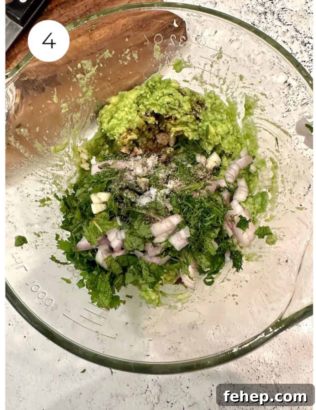 Mashed avocado in a bowl with chopped herbs and onion.