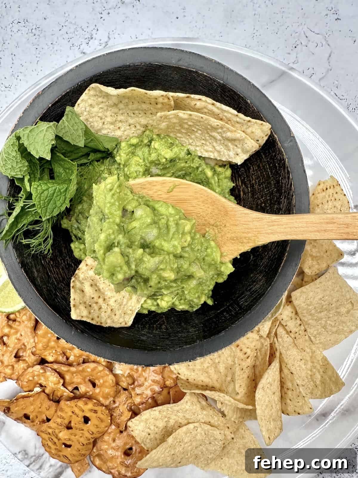 A spoon scooping up guacamole with chips and pretzel chips near the bowl.