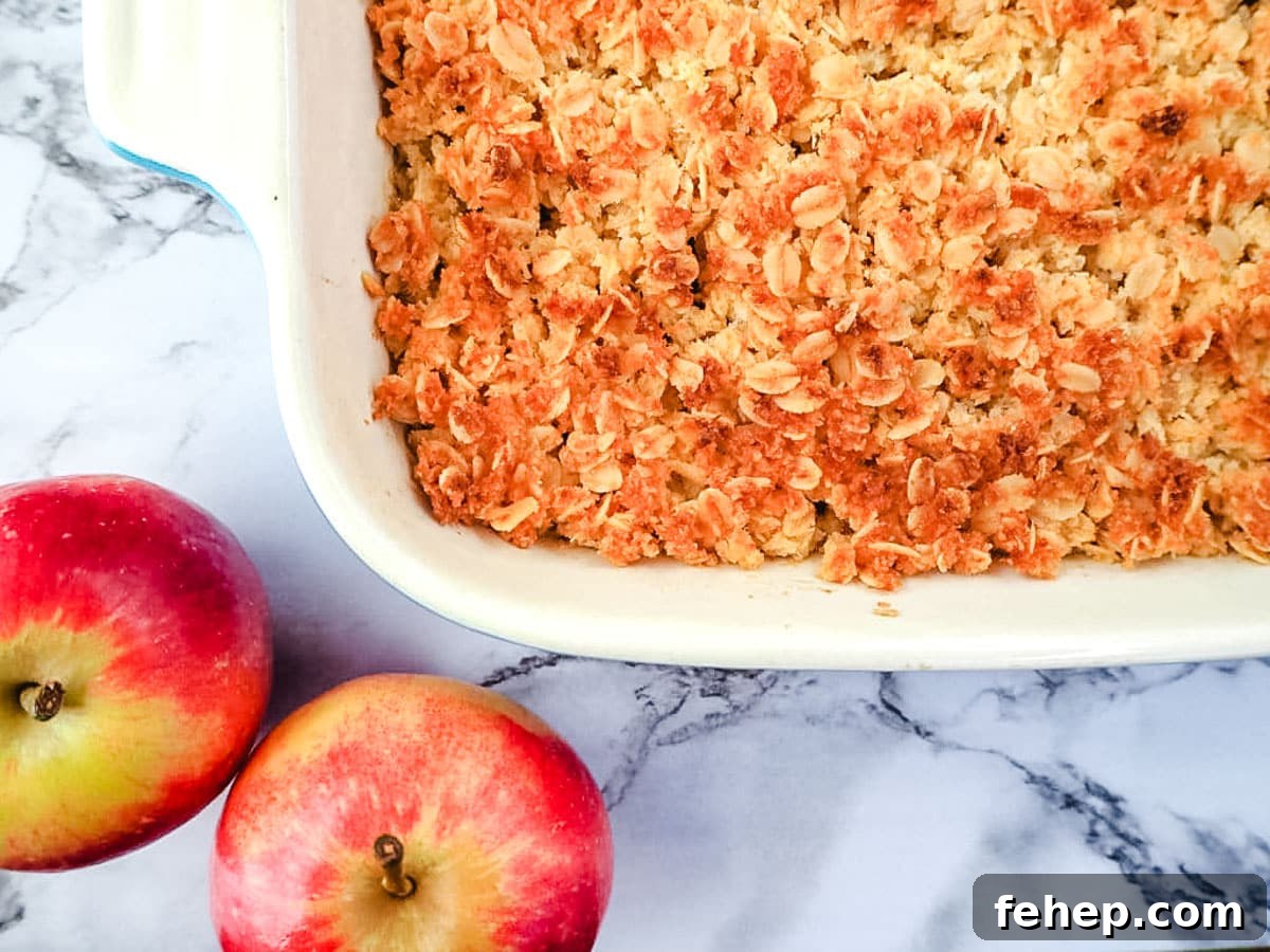 Baking dish of apple crumble with fresh apples on the side.