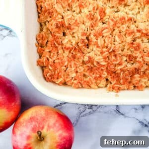 Baking dish of apple crumble with fresh apples on the side.