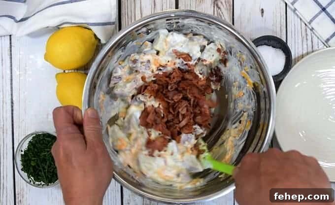 Creamy Bacon Ranch Potato Salad Recipe for Summer BBQs 4 A person stirring bacon into potato ranch salad