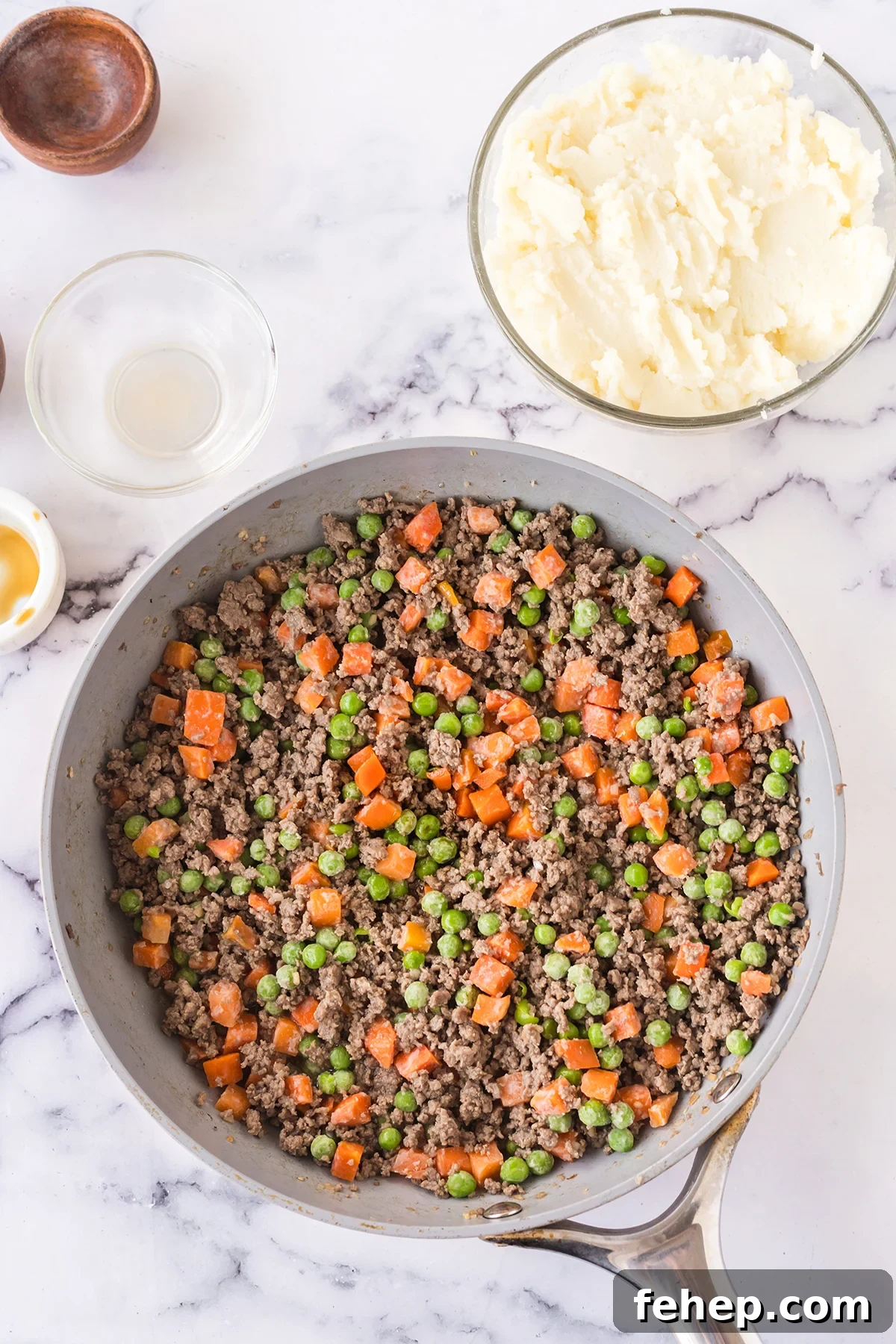 Cooked peas and carrots and browned ground beef in skillet.