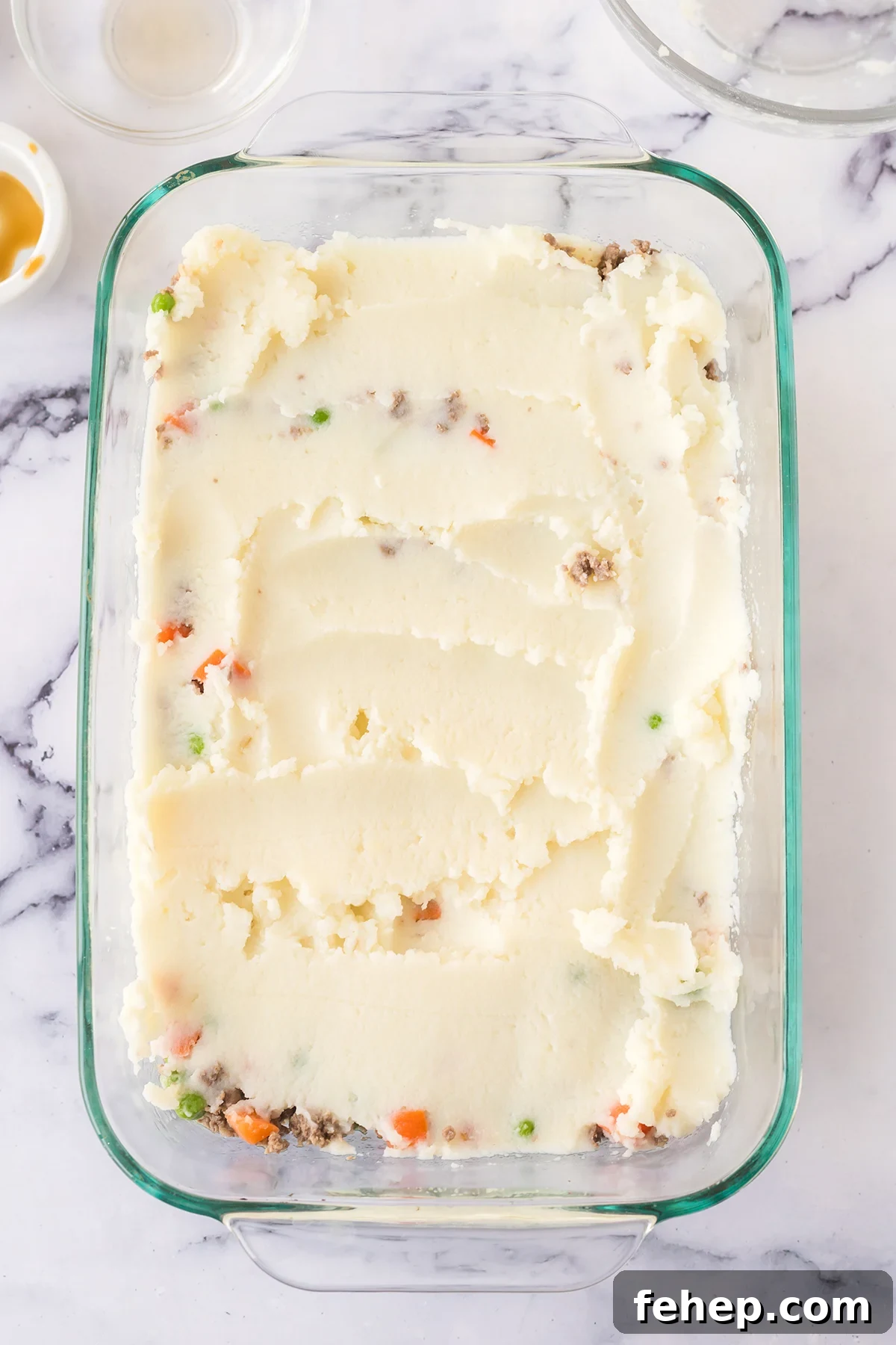 Ground beef mixture topped with mashed potatoes in baking dish.
