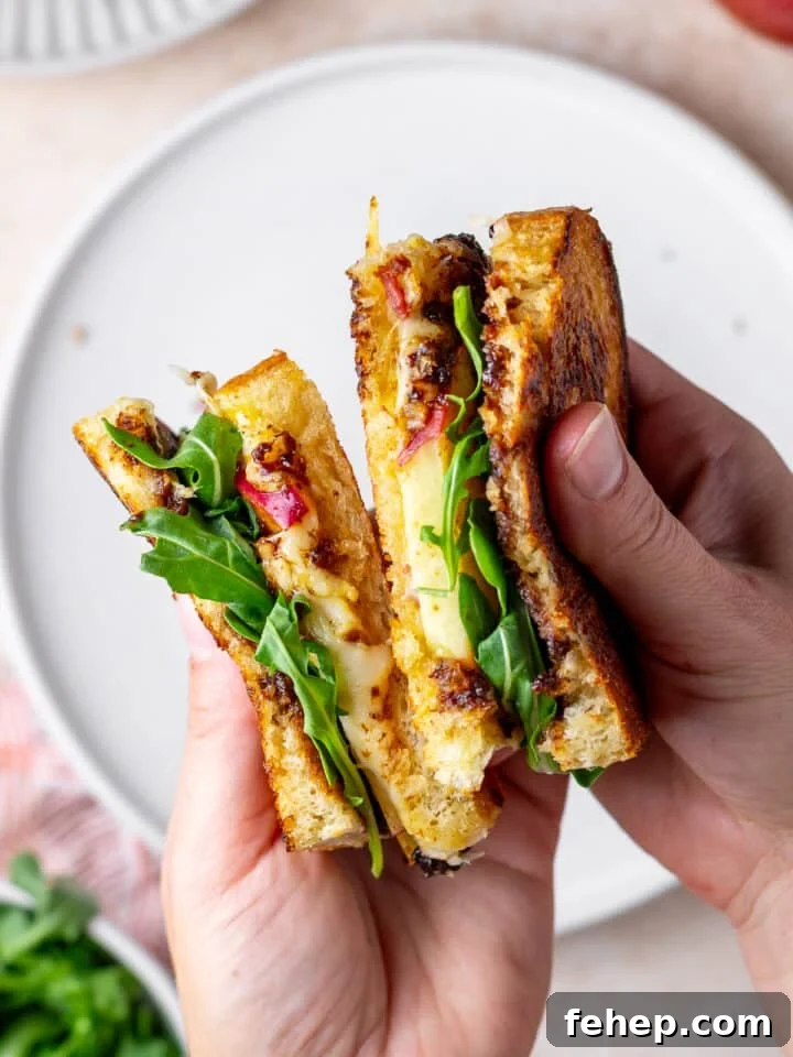 Gruyère Grilled Cheese with Fig Jam and Apple Slices 13 hands holding a grilled cheese sandwich that has Gruyere cheese, bacon, apple, fig jam and arugula