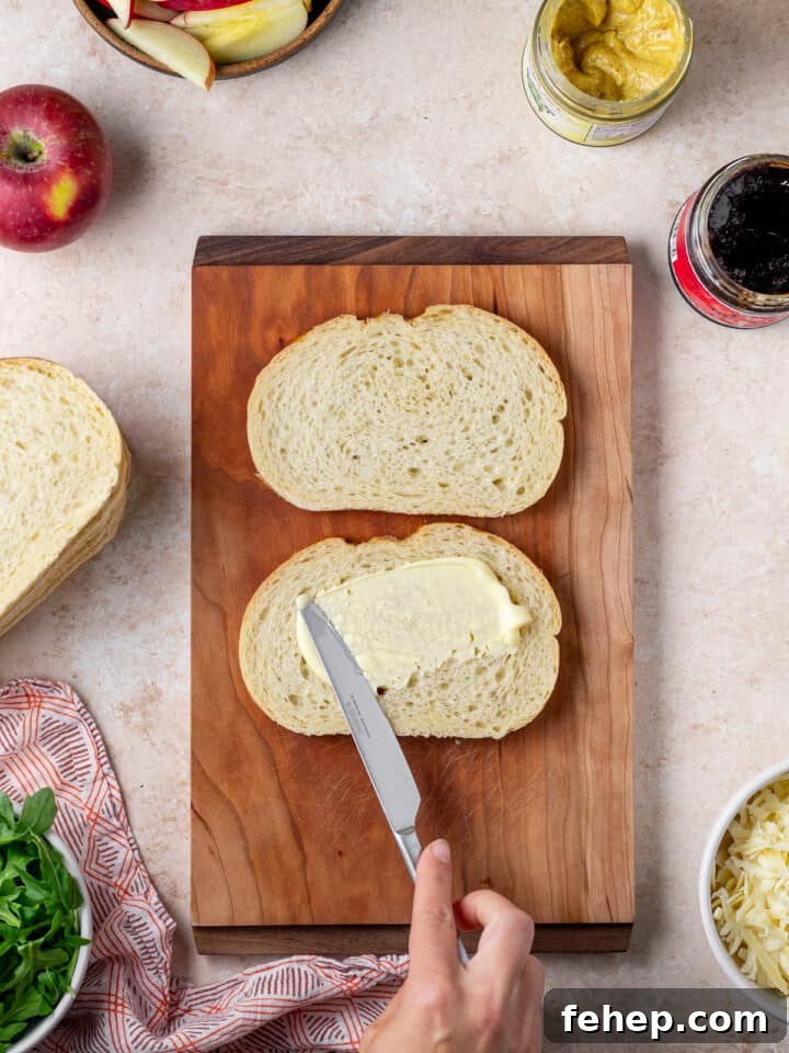 Gruyère Grilled Cheese with Fig Jam and Apple Slices 4 hand using a knife to spread mayo on the outside of two pieces of bread