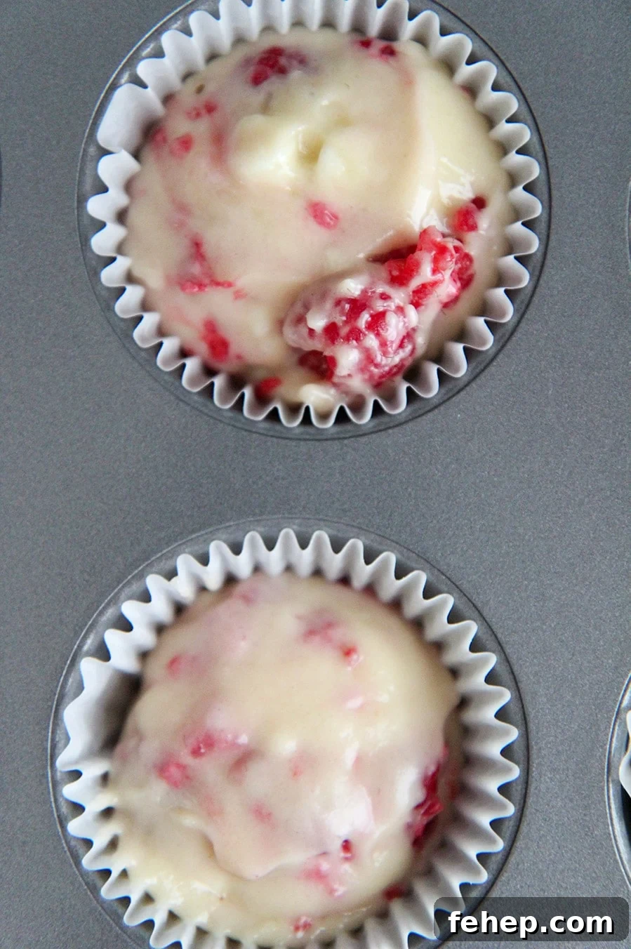 White Chocolate Raspberry Muffins Recipe with Luscious Berry Swirls 3 a muffin tin with two cupcake liners filled with batter.