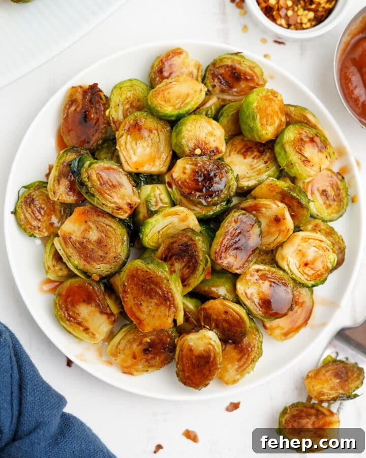 Honey sriracha brussels sprouts are served up on white plate with a fork next to it.