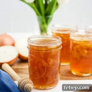A jar of honey onion cough syrup on the table in front of more jars and some onions.