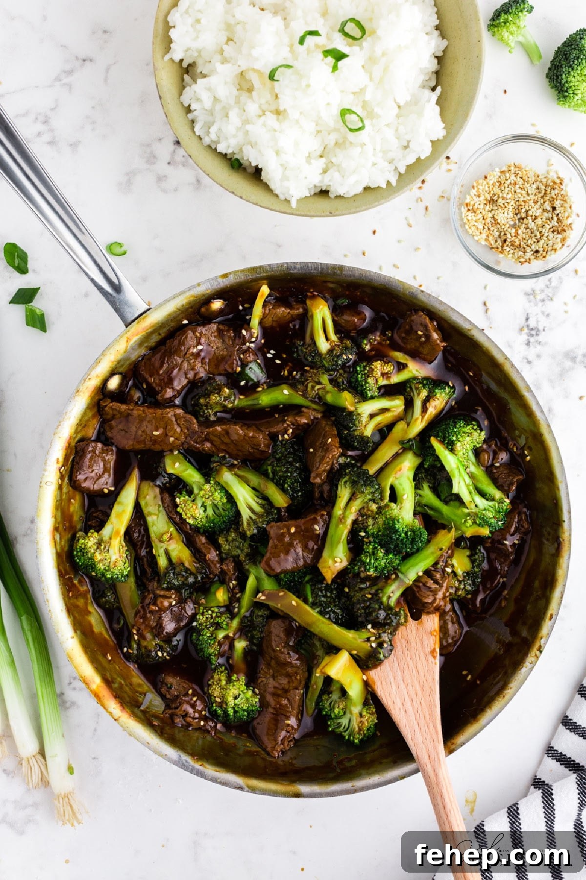 Panda Express Beef and Broccoli Recipe (Copycat Version) 12 Panda Express Beef and Broccoli in skillet, bowl of rice, bowl of toasted sesame seeds, and wooden serving utensil.