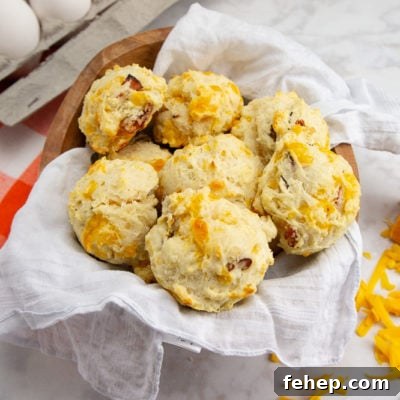 Savory Ham and Cheese Biscuit Recipe for Breakfast or Brunch 7 Ham and cheddar biscuits in a bowl beside cheddar cheese and eggs on a white table
