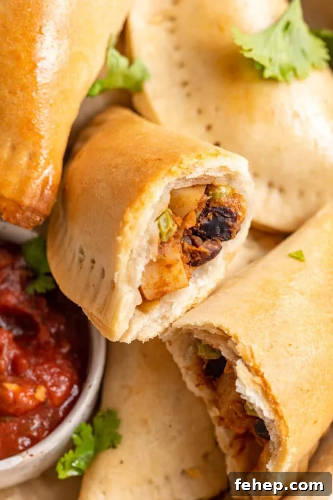 Vegan Empanadas: Flavorful Plant-Based Empanada Recipes 2 Overhead view of a pile of vegan empanadas next to a small bowl of salsa, with one empanada torn in half to show insides.