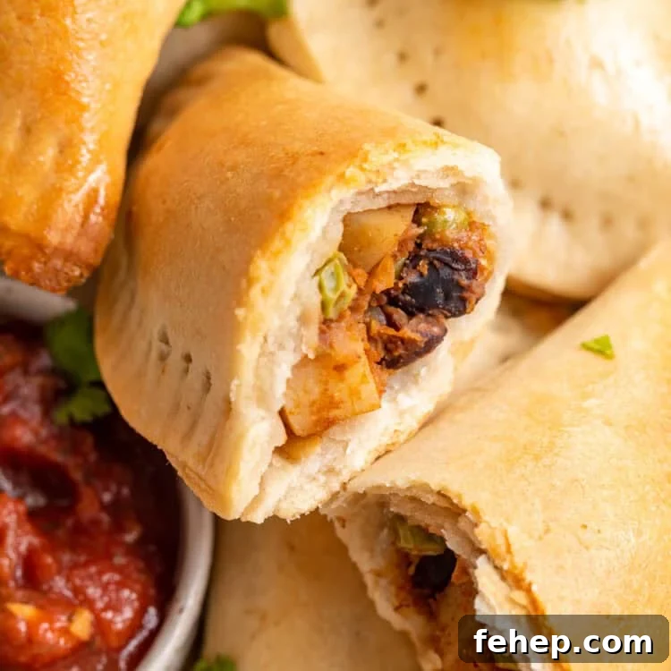Vegan Empanadas: Flavorful Plant-Based Empanada Recipes 4 Overhead view of a pile of vegan empanadas next to a small bowl of salsa, with one empanada torn in half to show insides.