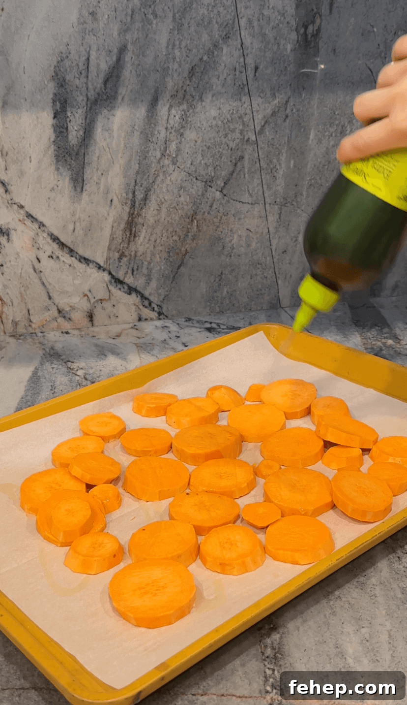 Sweet potato rounds on sheetpan with olive oil being drizzled