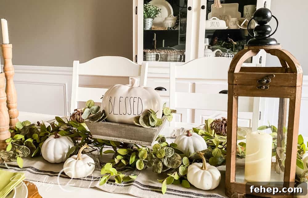 close up of rae dunn pumpkin in wood pedastal bowl with greenery and mini pumpkins on table