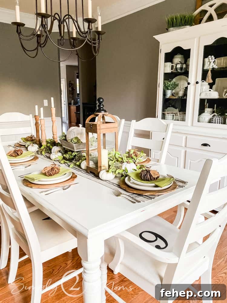 table set with neutral wood candle holders and greenery in dining room with china hutch to left side of table