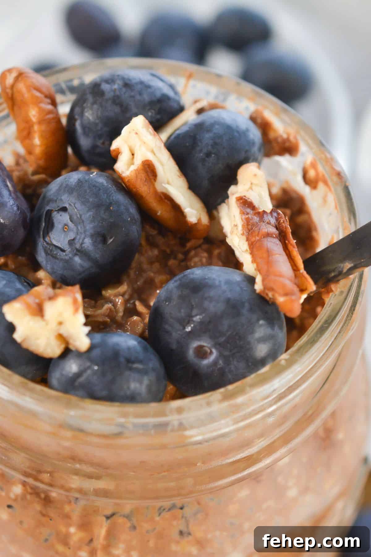 A jar with fresh blueberries and pecan pieces, with a spoon inside.