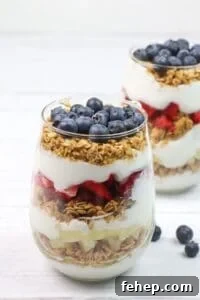 A glass filled with layers of granola, strawberries, and blueberries creates a delicious dessert.