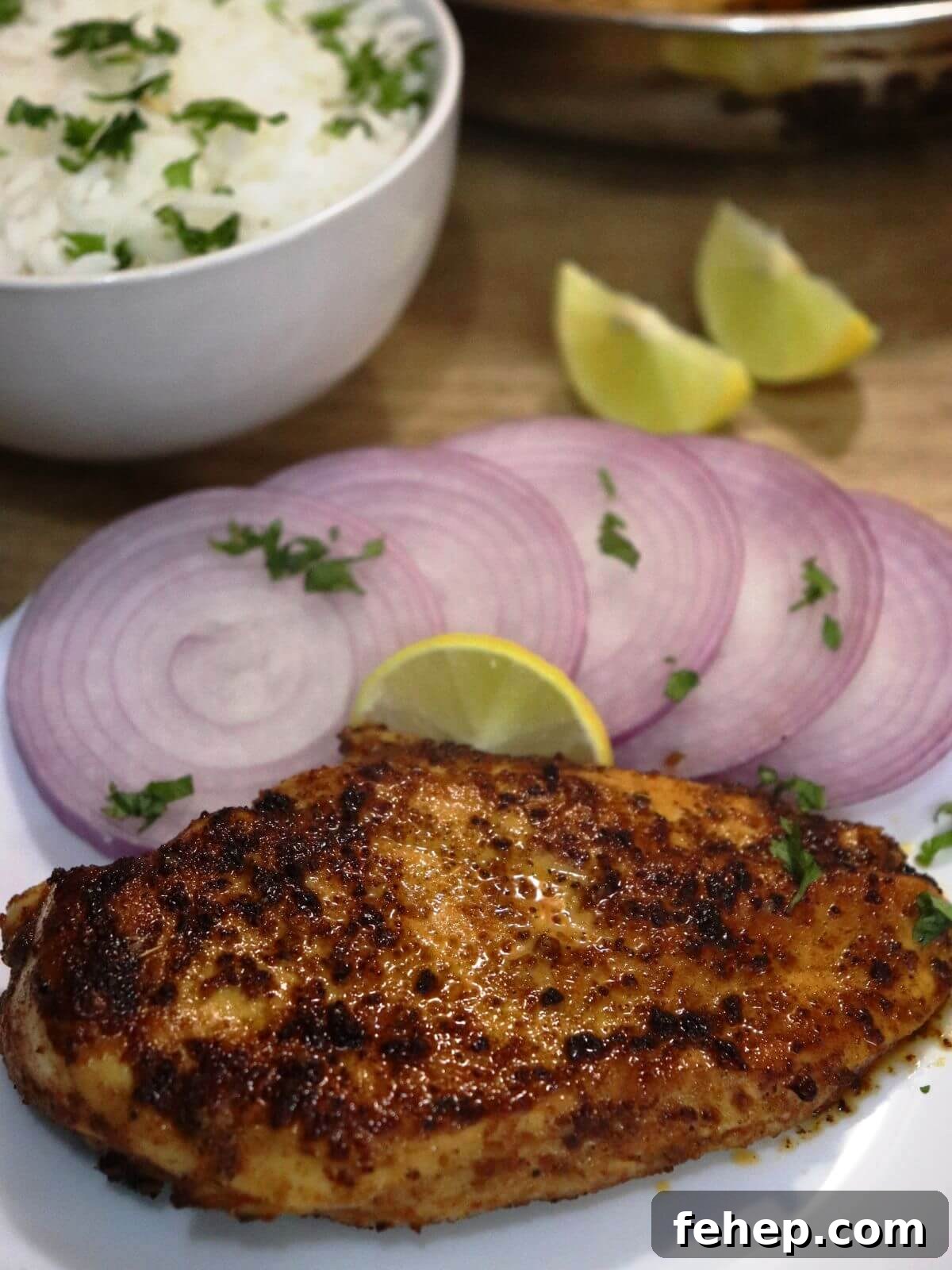 close-up of cumin chicken served in a plate with onion slices and a lemon wedge.