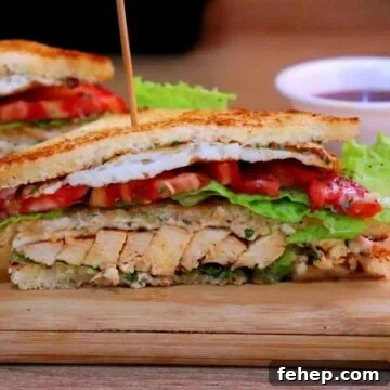 chicken club sandwich sliced in half and placed on a board.