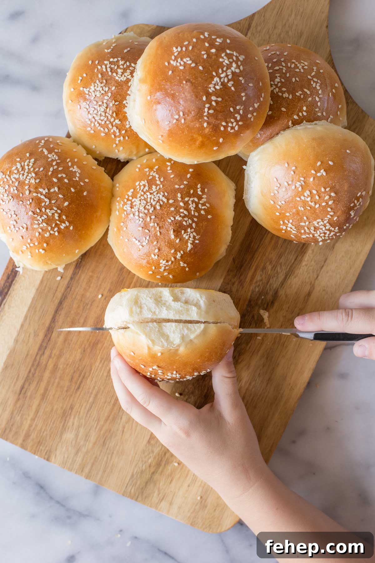 Homemade Sourdough Hamburger Buns for Tender, Tangy Burgers 4 A Sourdough Hamburger Bun being cut open on a wooden cutting board with more buns next to it.