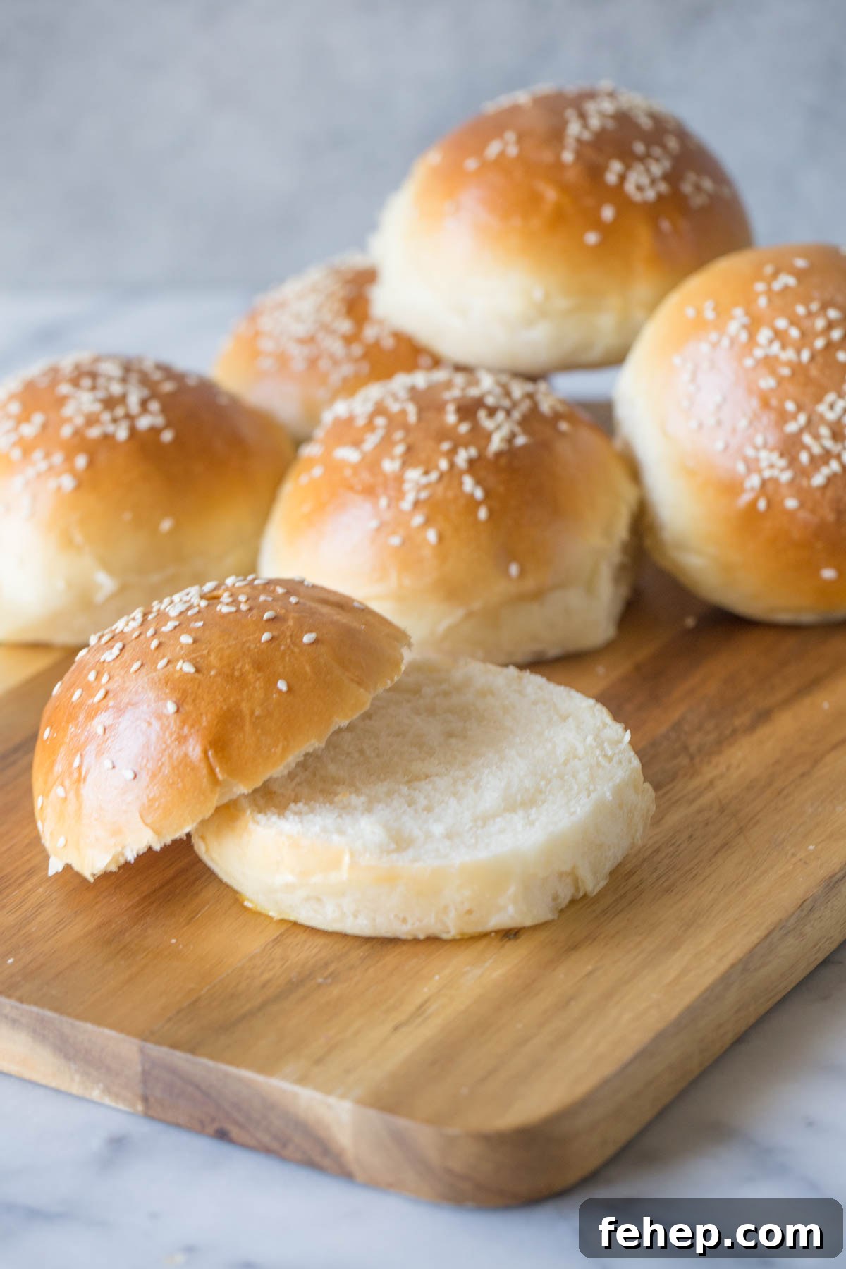 Homemade Sourdough Hamburger Buns for Tender, Tangy Burgers 7 Sourdough Hamburger Buns on a wooden cutting board.