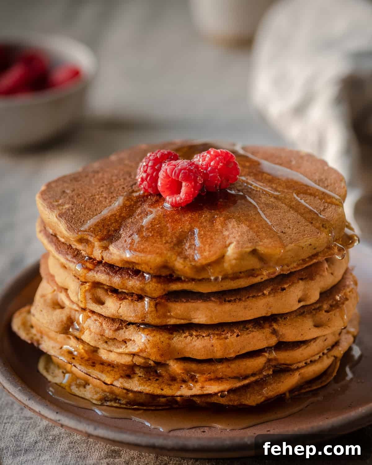 vegan pumpkin pancakes with maple syrup and raspberries on linen tablecloth