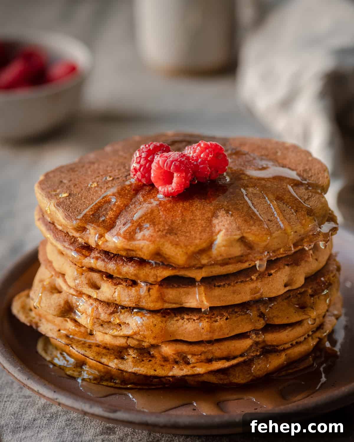 vegan pumpkin pancakes with maple syrup and raspberries on linen tablecloth