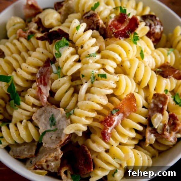 Overhead image of creamy pasta with sausage and bacon in a white bowl.