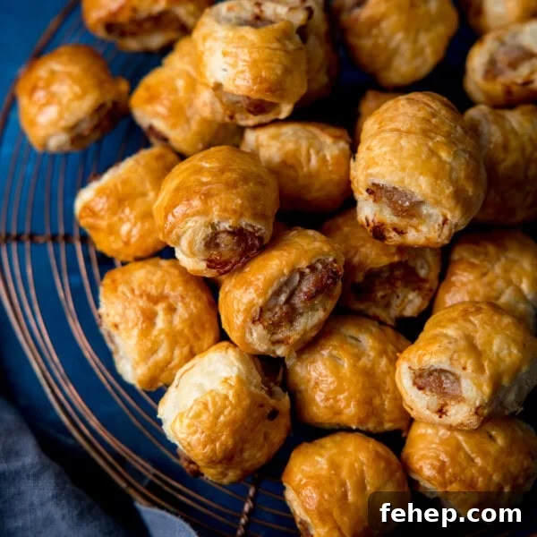 A pile of golden-brown sausage rolls rests on a wire cooling tray, showing flaky pastry and browned meat filling.