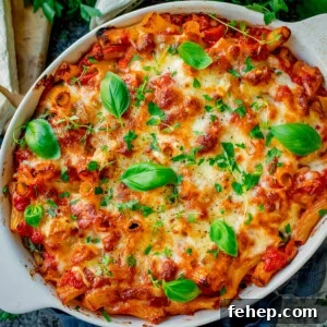 Sausage Pasta Bake topped with melted cheese and fresh basil leaves in a white oval dish.