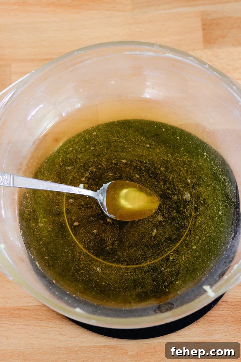 Lotion bar ingredients in a glass bowl, completely melted with a spoon in the bowl.